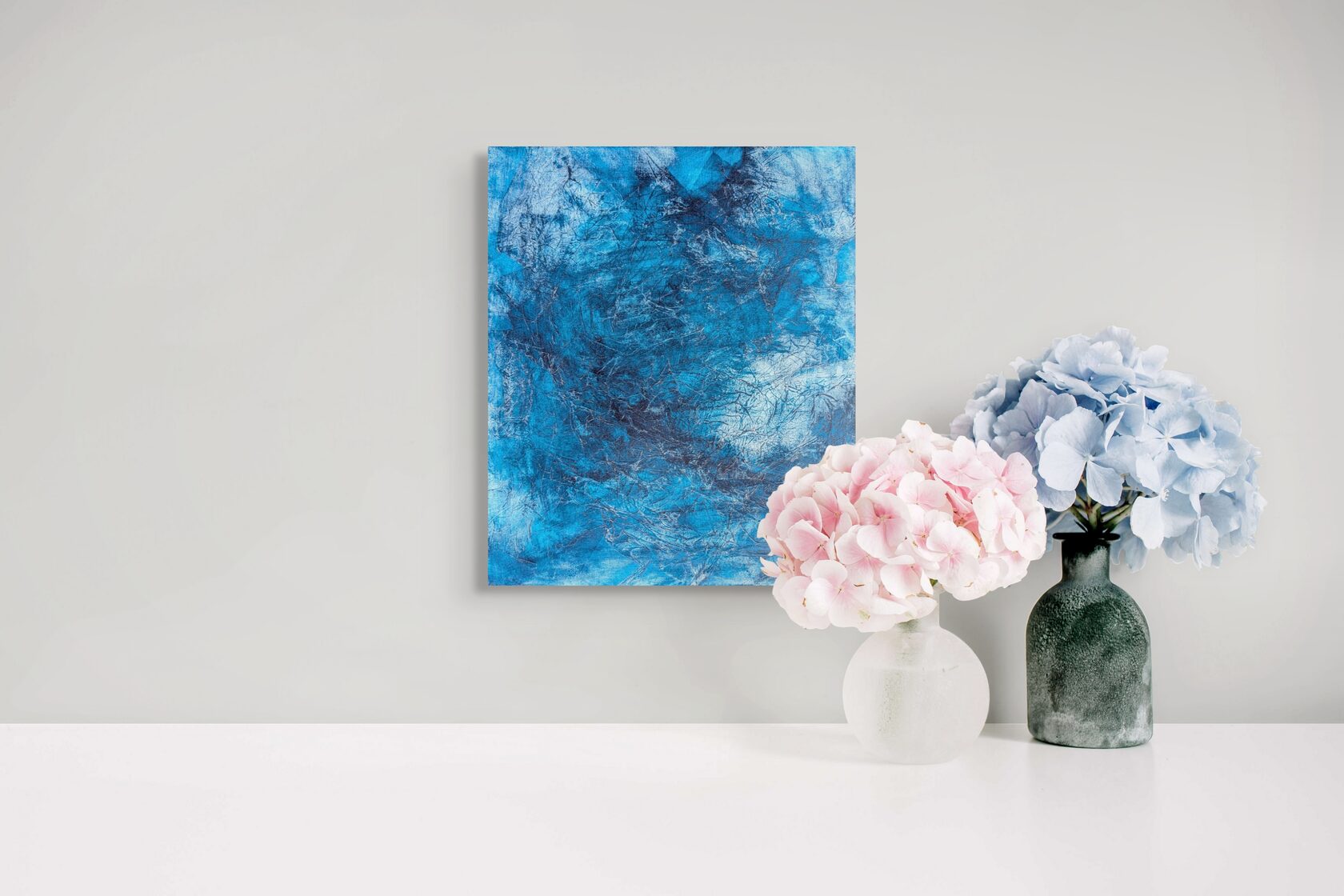a white table with two vases of flowers and a painting hanging on the wall above them.