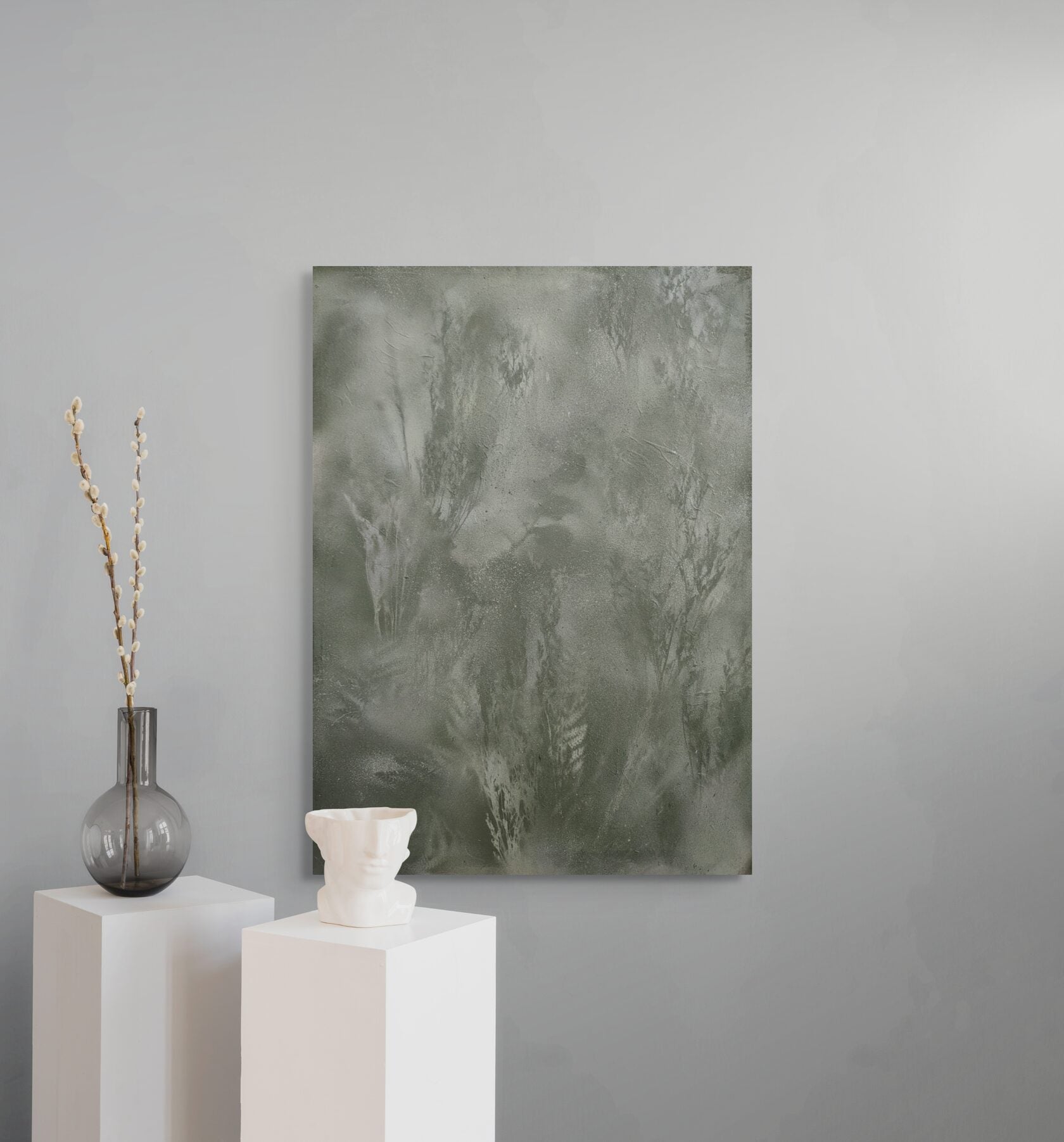a minimalist setting with a large abstract painting on a gray wall, a white vase with branches, and a white sculpture on a white pedestal.