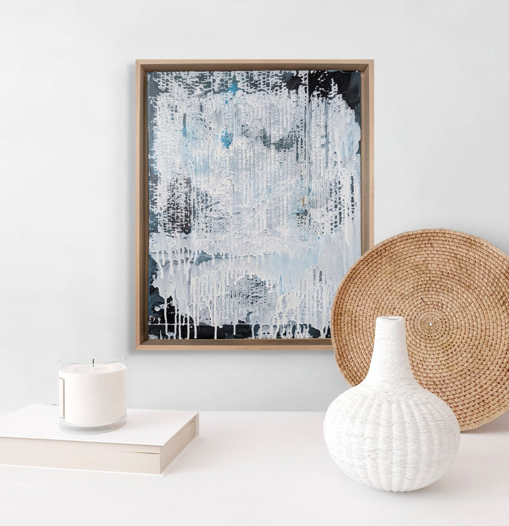 Framed abstract art piece on a wall with a white vase and woven basket below.