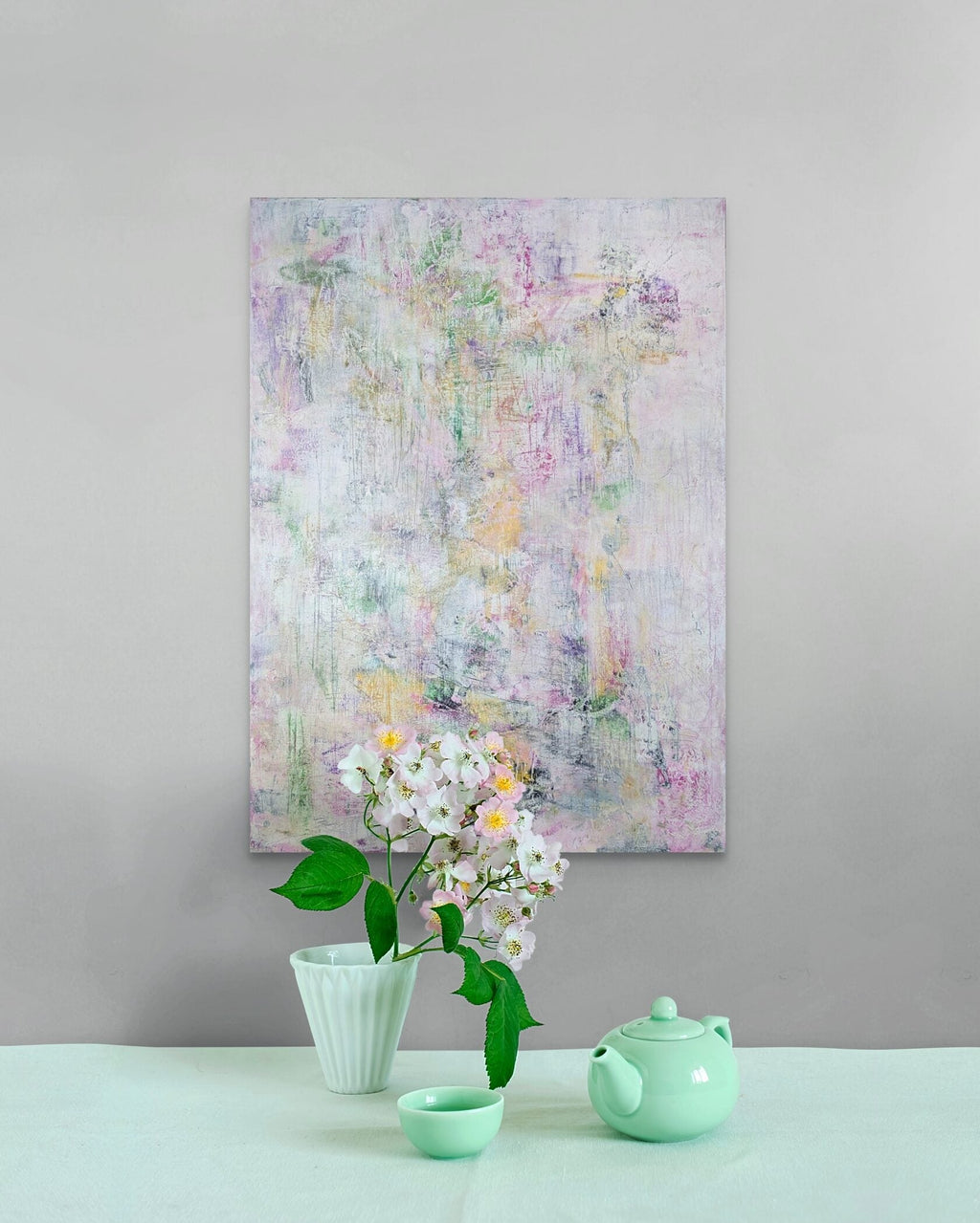 Abstract floral painting on a gray wall with a green teapot and cup below.