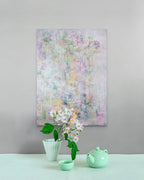 Abstract floral painting on a gray wall with a green teapot and cup below.
