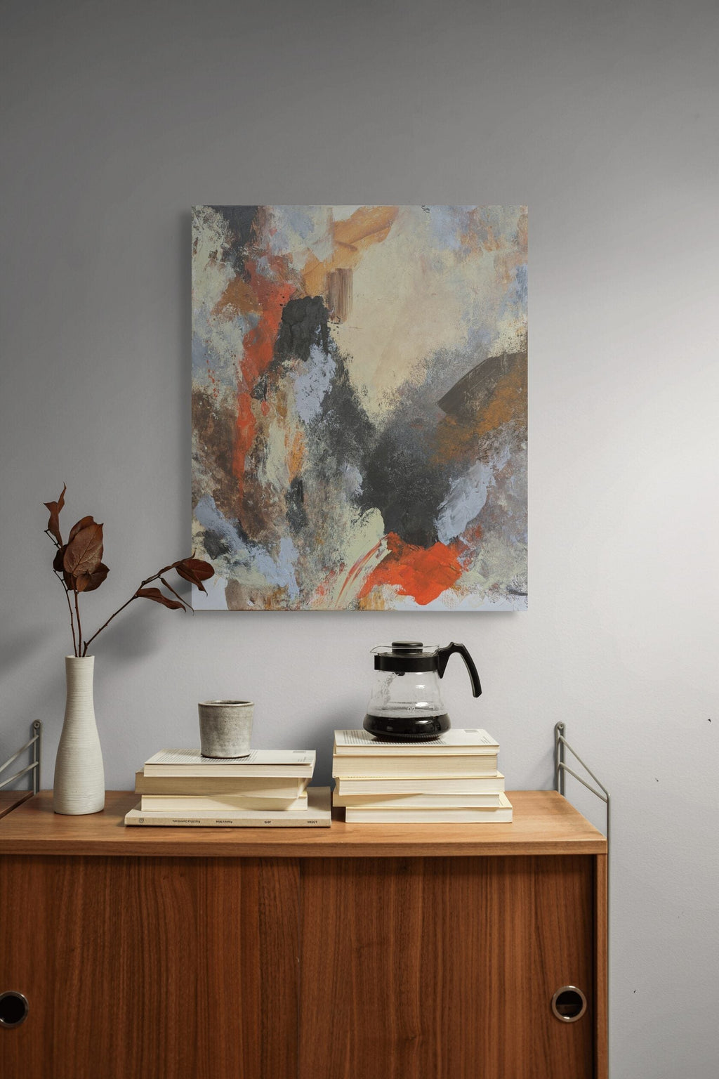 Abstract painting above a wooden cabinet with books and a coffee maker.