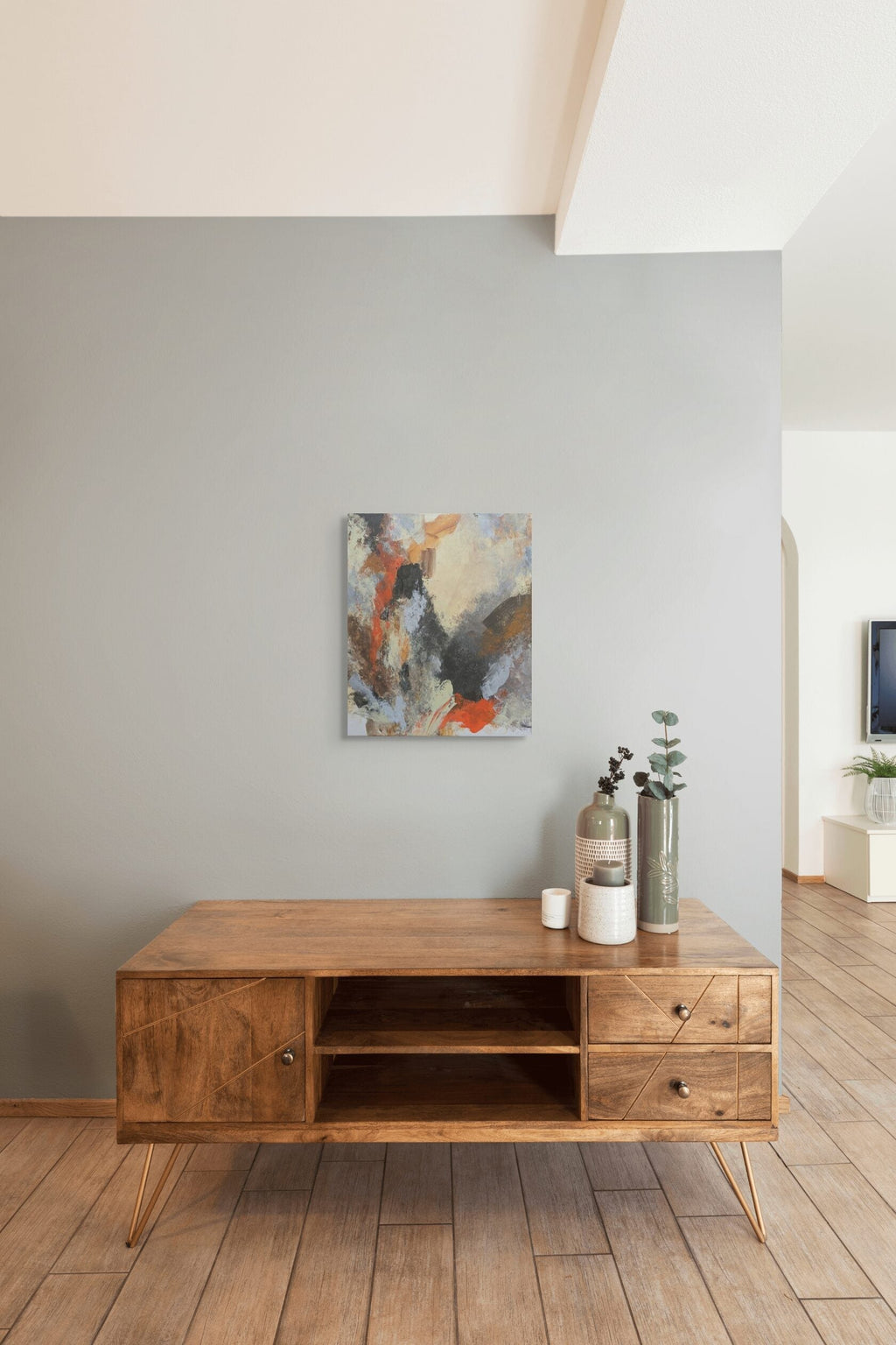Wooden TV stand with decorative items against a gray wall with abstract art.