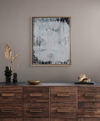 Wooden dresser with abstract art and decorative items against a gray wall