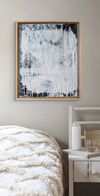 Abstract painting in a wooden frame on a wall above a bed.