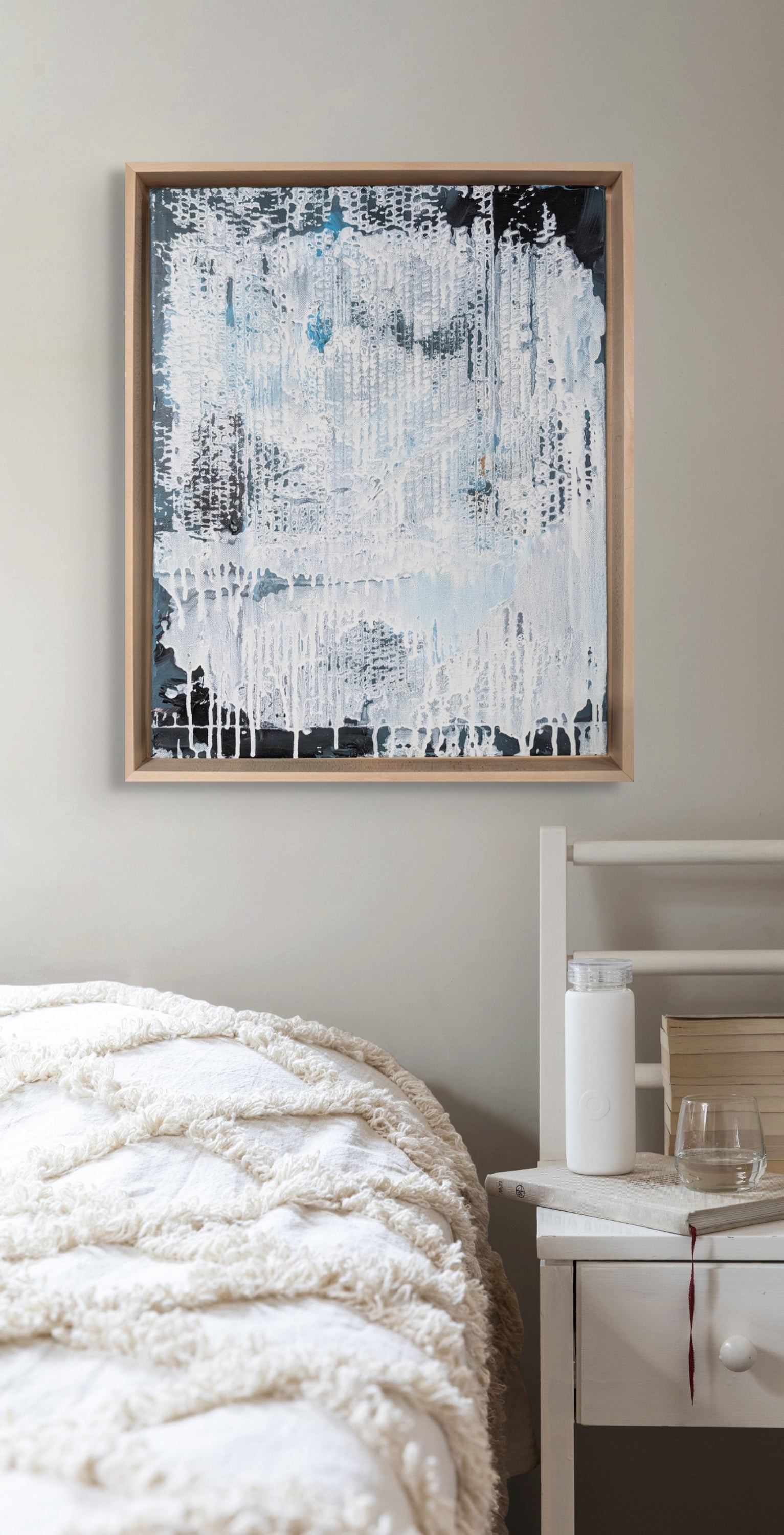 Abstract painting in a wooden frame on a wall above a bed.