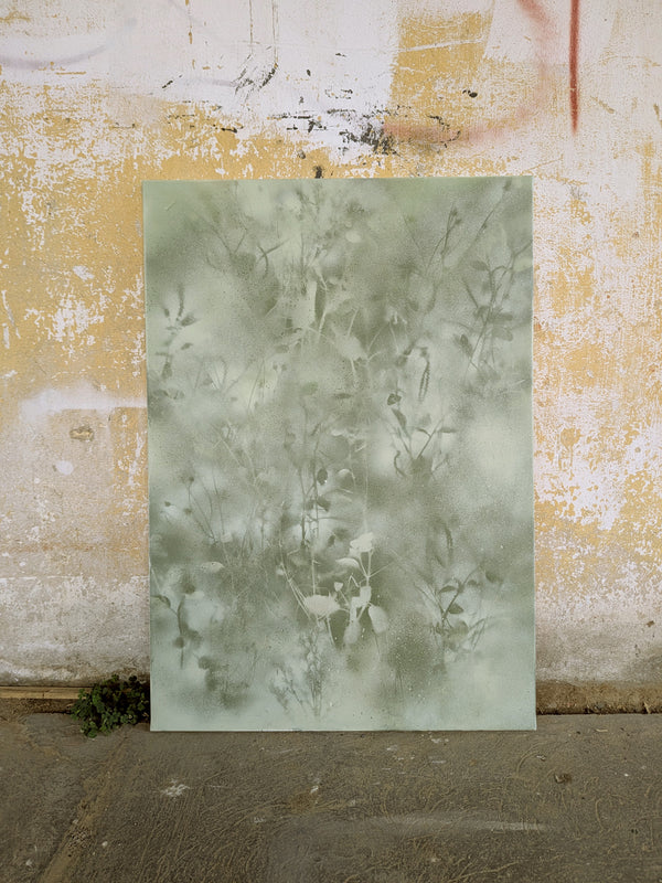 a large, square-shaped piece of paper or canvas with a greenish-gray, textured pattern or design on it, set against a weathered, yellow-painted wall.