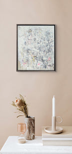 Framed abstract art on a beige wall with a table displaying a vase, candle, and books.