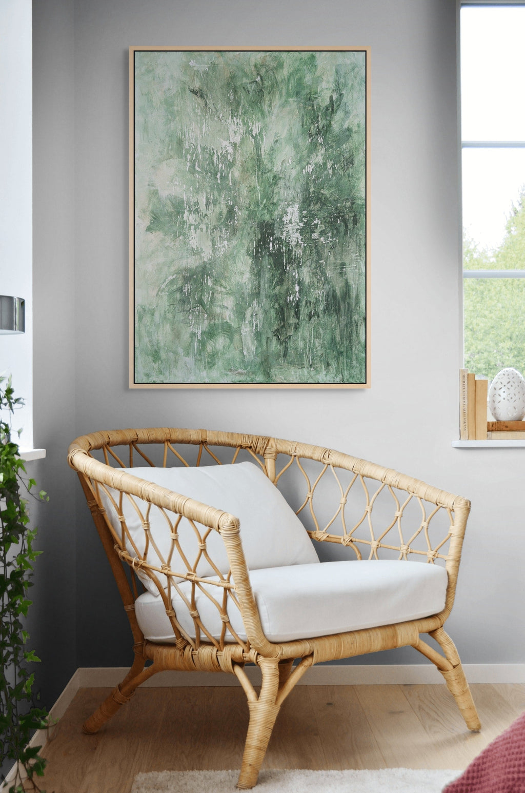 Rattan chair with white cushions in a room with a large abstract green painting on the wall.