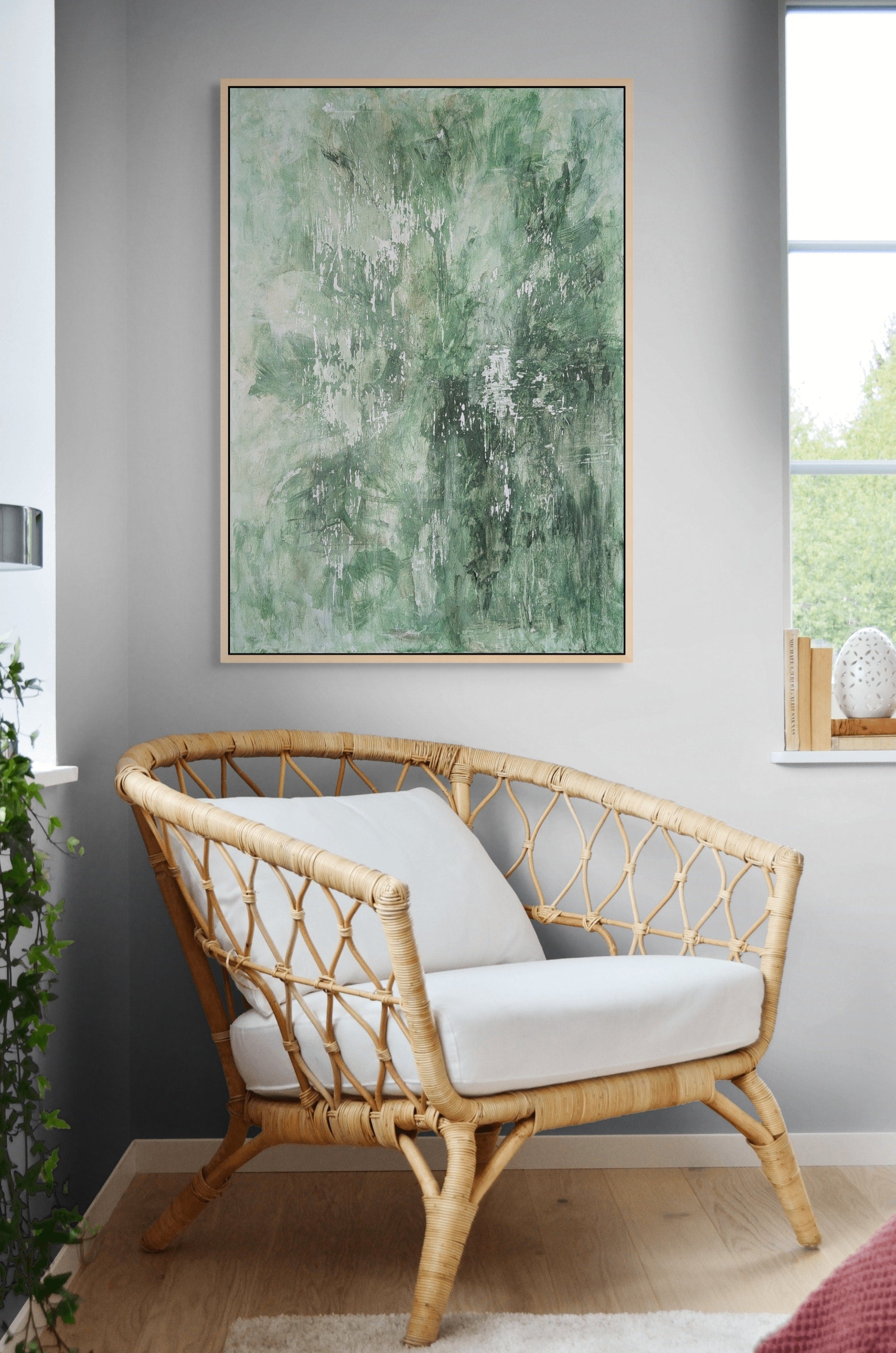 Rattan chair with white cushions in a room with a large abstract green painting on the wall.