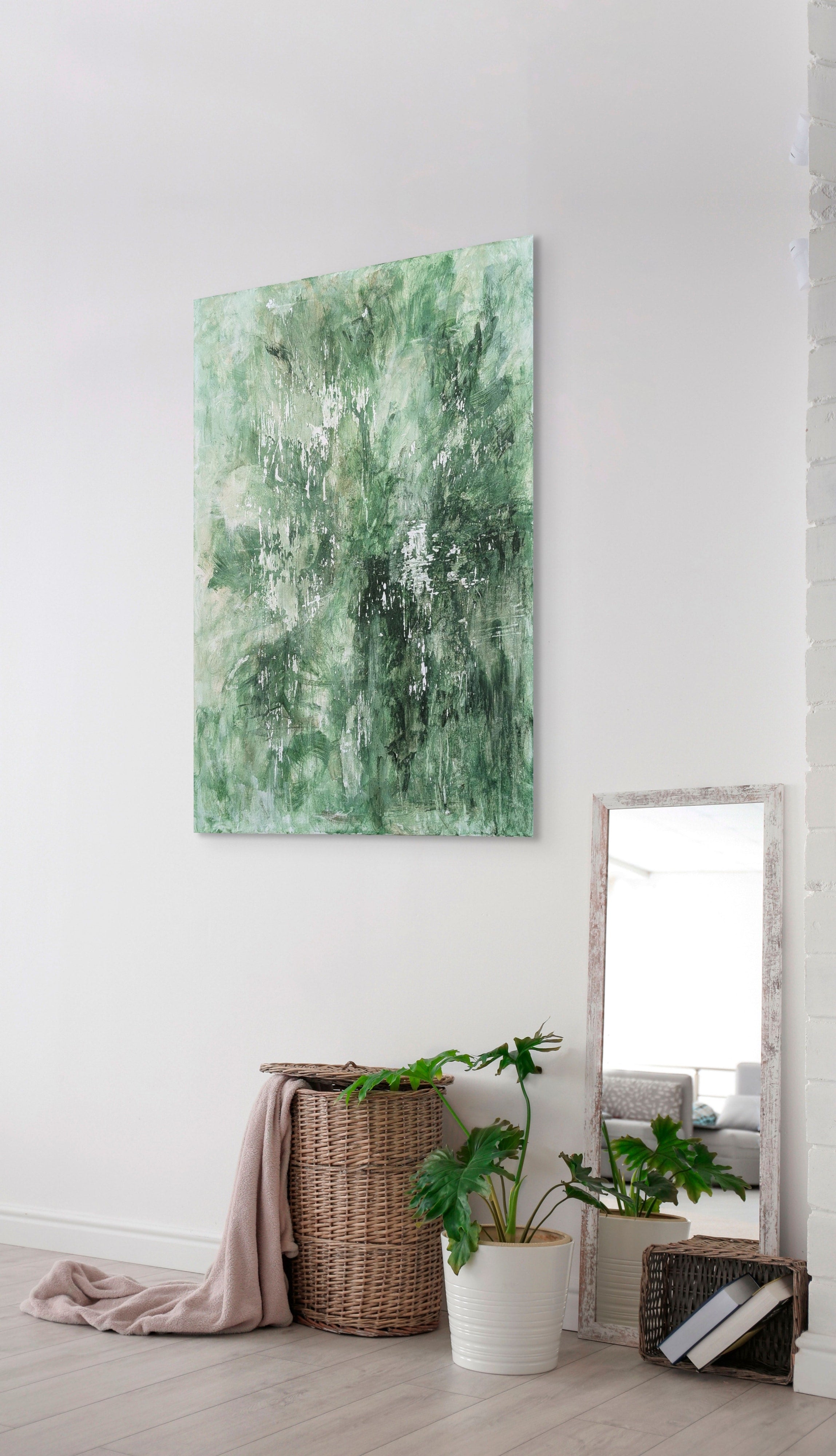 Abstract green painting on a white wall with a mirror and plants below.