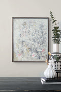 Abstract painting in a black frame on a wall above a dark surface with decorative items.