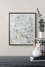Abstract painting in a black frame on a wall above a dark surface with decorative items.