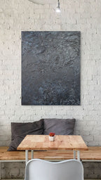 Abstract painting on a white brick wall above a wooden table with a plant and pillows.